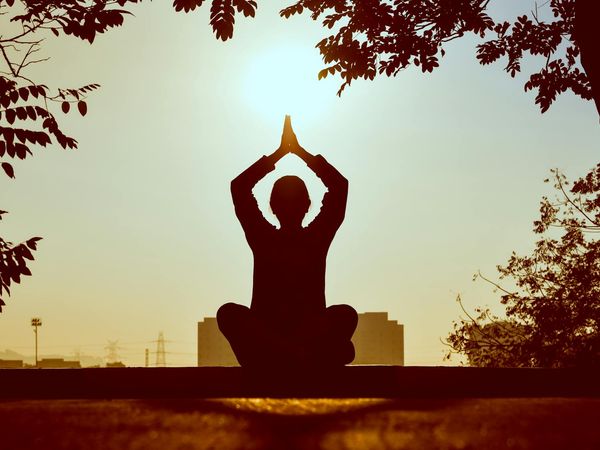 Silhouette of a person meditating during sunrise with bordeaux tones.